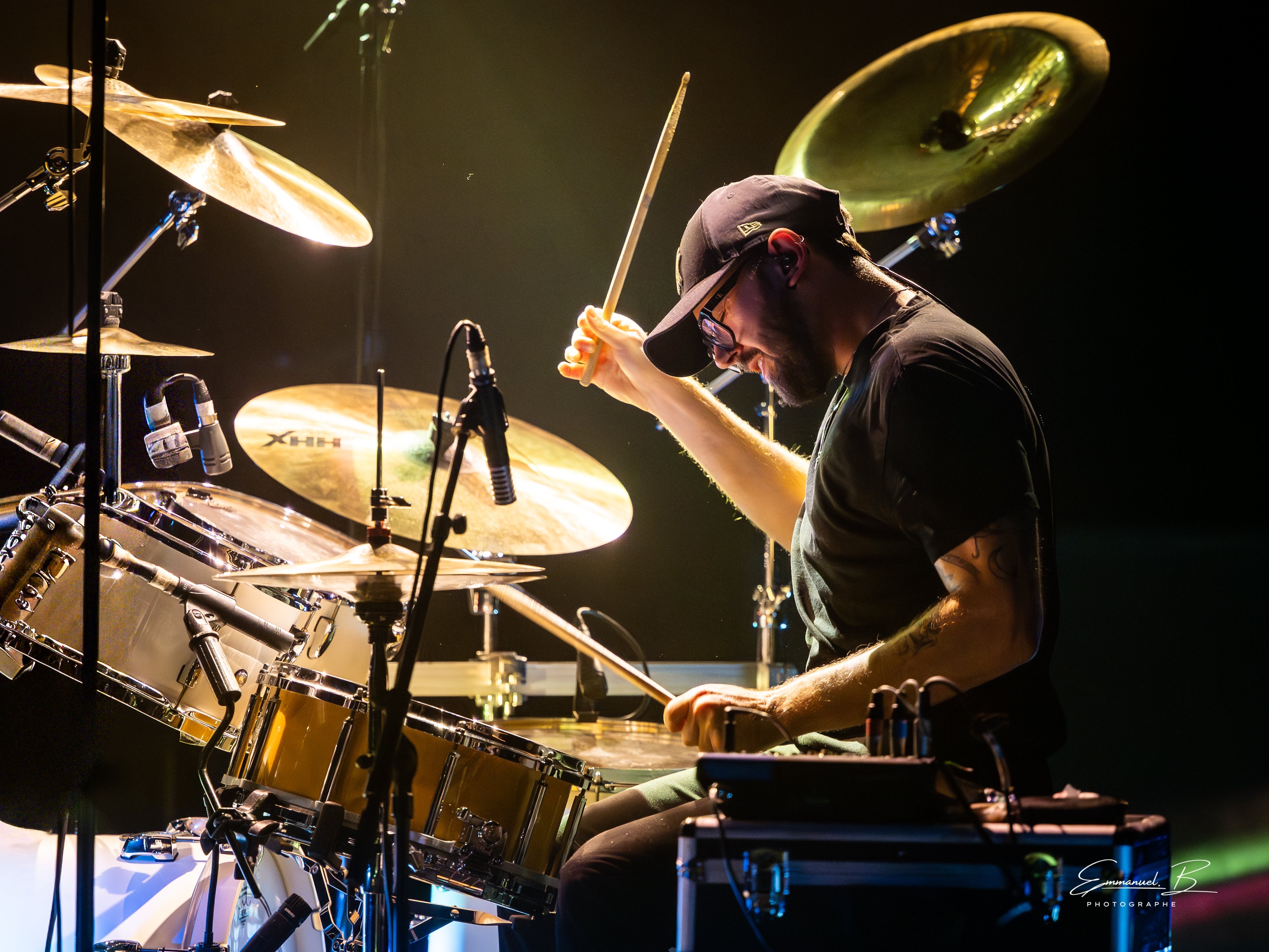 Batteur en concert, bras levés au-dessus des cymbales, derrière son kit